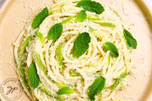 An overhead view looking down onto a nest of pasta on a plate, garnished with fresh mint leaves.