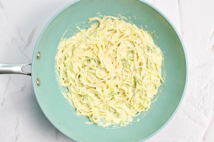 Spaghetti pasta mixed into creamy zucchini in a skillet.