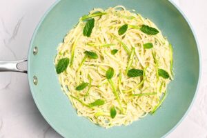 Fresh mint leaves added to creamy pasta in a skillet.