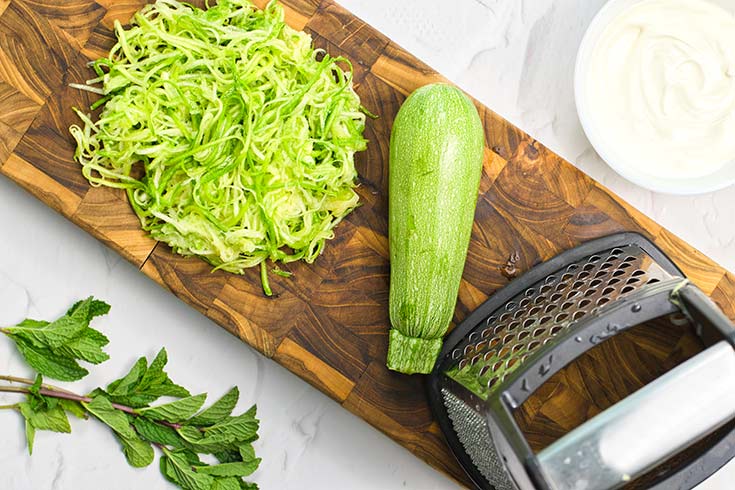 Grated zucchini on a cutting board next to a grater.