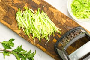 Julienned zucchini on a cutting board next to a grater,