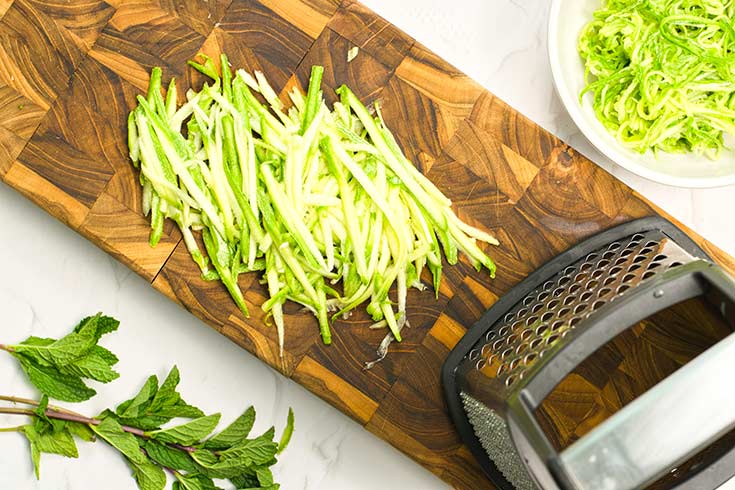 Julienned zucchini on a cutting board next to a grater,