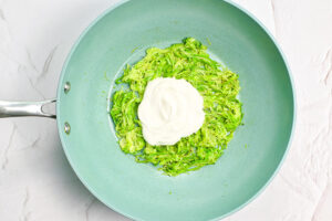 Cream added to cooked zucchini in a skillet.