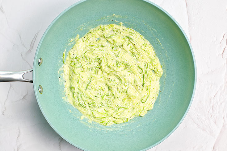 Zucchini pasta mixed with cream in a skillet.