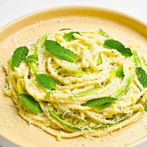 A plate holds a nest of spaghetti pasta garnished with mint leaves and parmesan cheese.