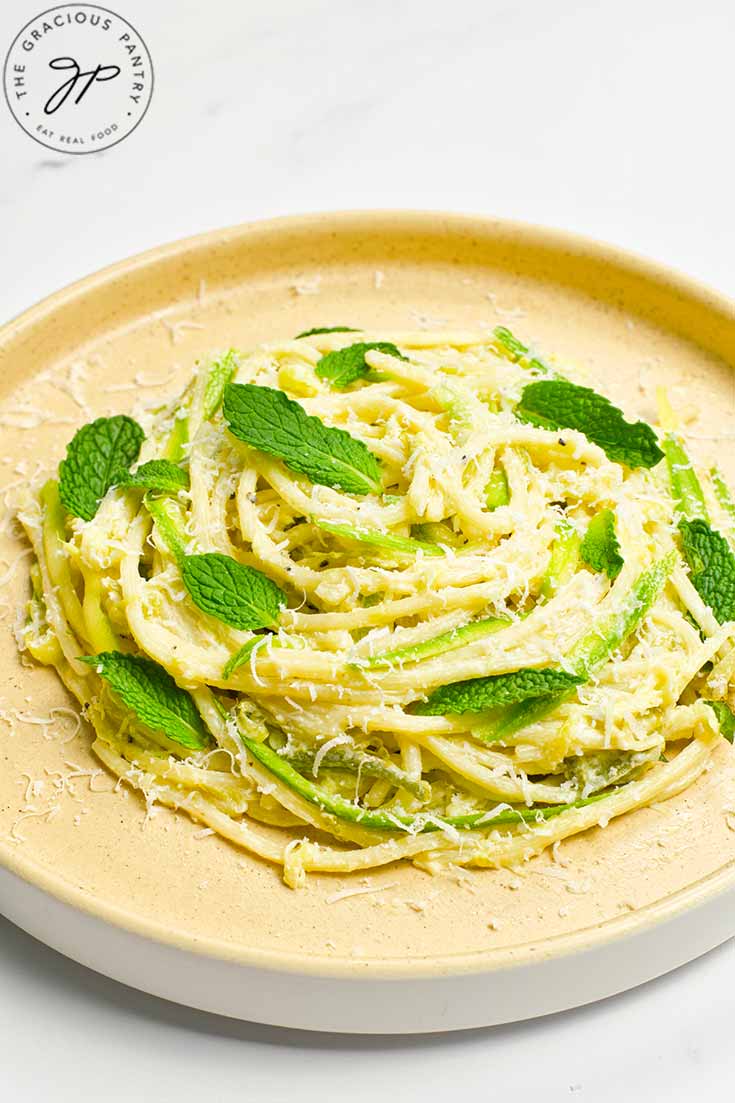 A plate holds a nest of spaghetti pasta garnished with mint leaves and parmesan cheese.