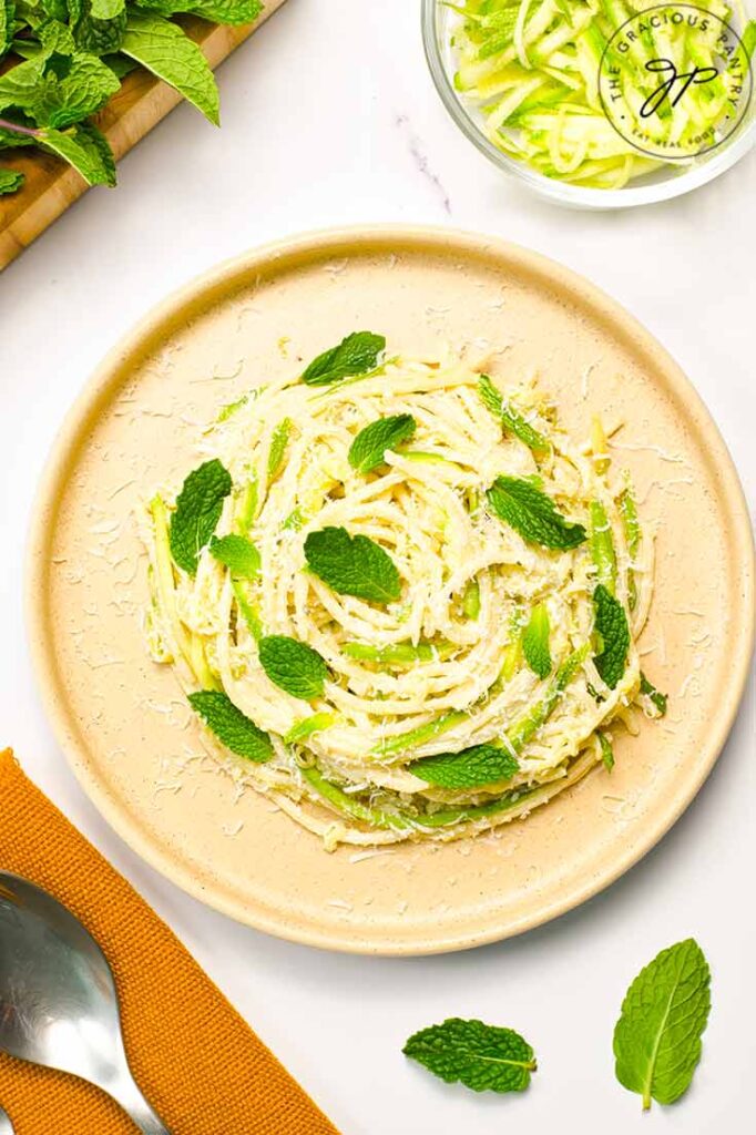 An overhead view of a plate holding a nest of spaghetti pasta garnished with parmesan and fresh mint leaves.