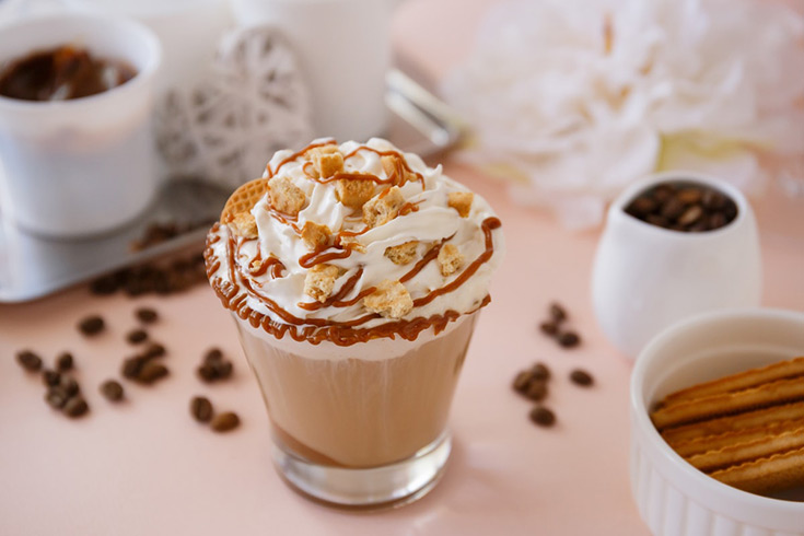 A caramel brulee latte garnished with whipped cream, syrup and cookie crumbs.