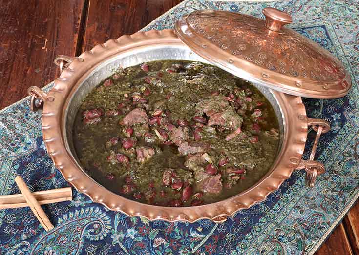 A copper dish filled with Ghormeh Sabzi sitting on a table.