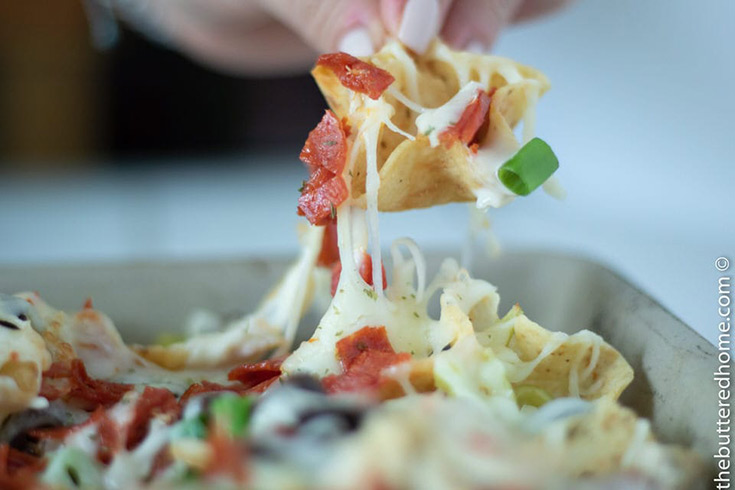A hand lifts a cheesy chip from a sheet pan full of Italian nachos.