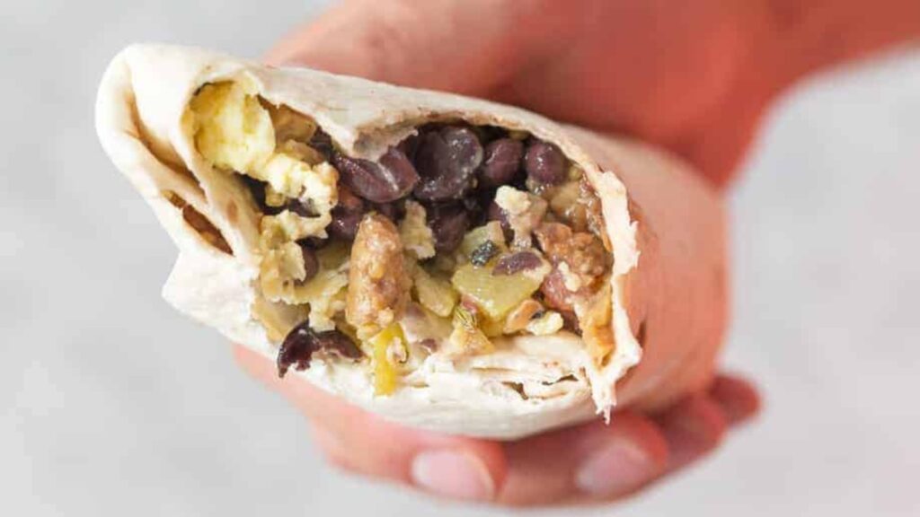 A hand holds a make ahead breakfast burrito with a bite taken out of it.