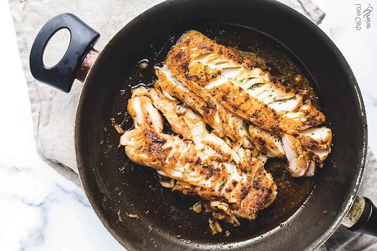 A black skillet with two cooked cod filets.