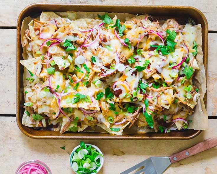 A sheet pan covered with BBQ pulled pork nachos.