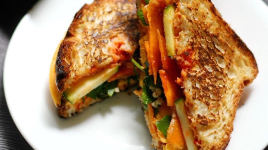 A vegan grilled cheese with veggies on a white plate.