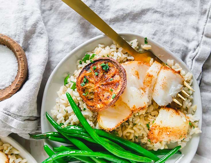 A plate of air fryer cod on a bed of rice with a side of green beans.
