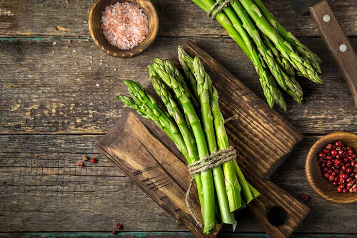 Two bunches of asparagus laying on a wood surface.