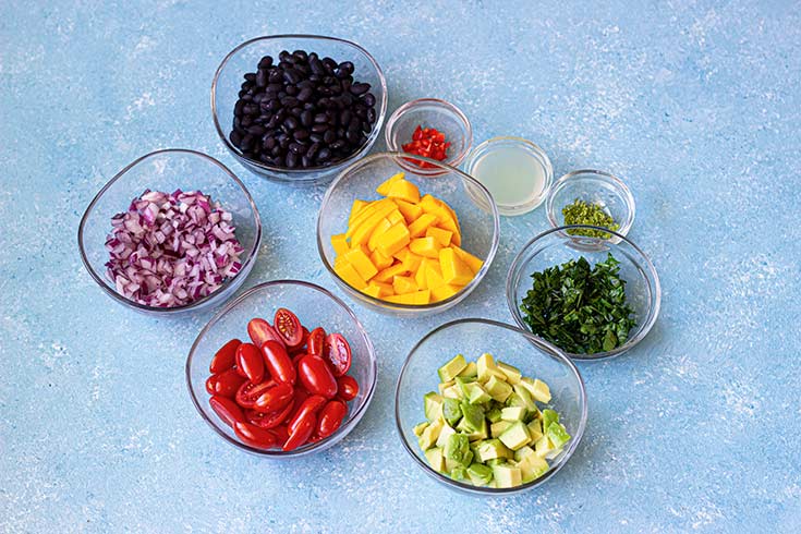 Black bean salad ingredients in individual bowls on a blue surface.