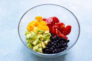 Beans, avocados, tomatoes and mango added to a mixing bowl.