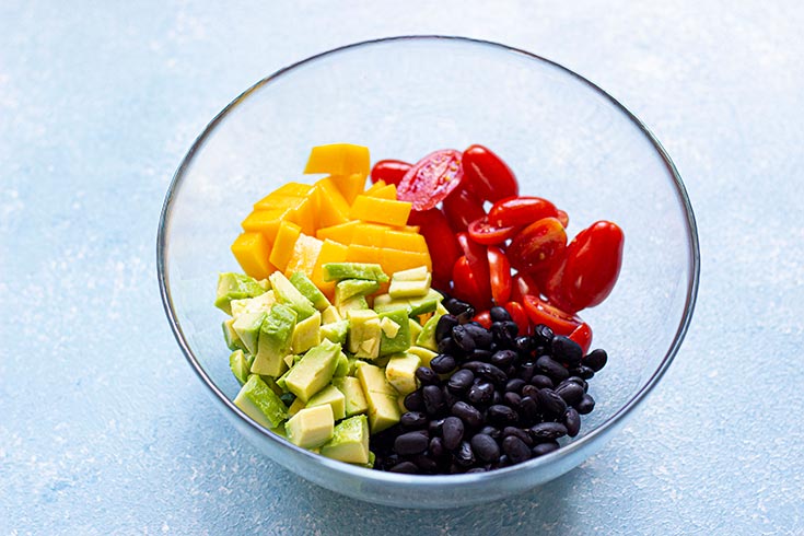 Beans, avocados, tomatoes and mango added to a mixing bowl.