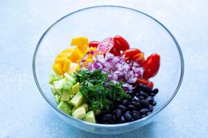 Herbs and onions added to a bowl of black bean salad ingredients.