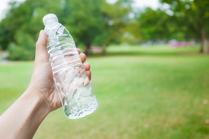 A hand holds up a single-use bottle of water.