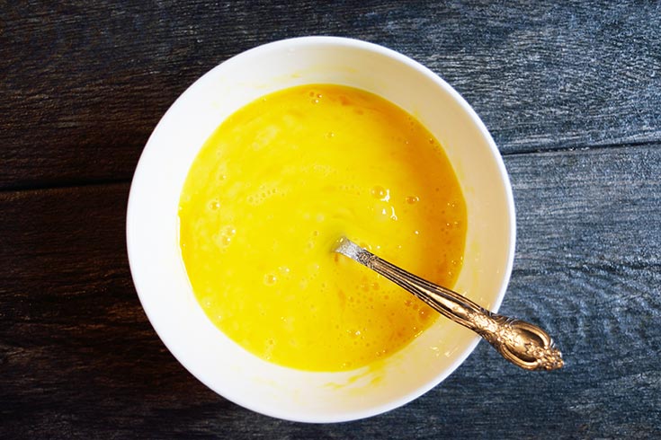 Eggs whisked in a white bowl with a fork.