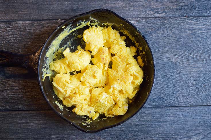 Scrambled eggs in a black skillet.