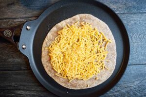 Grated cheese sprinkled over a tortilla on a skillet.