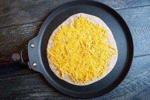 Half melted cheese on a quesadilla in a skillet.