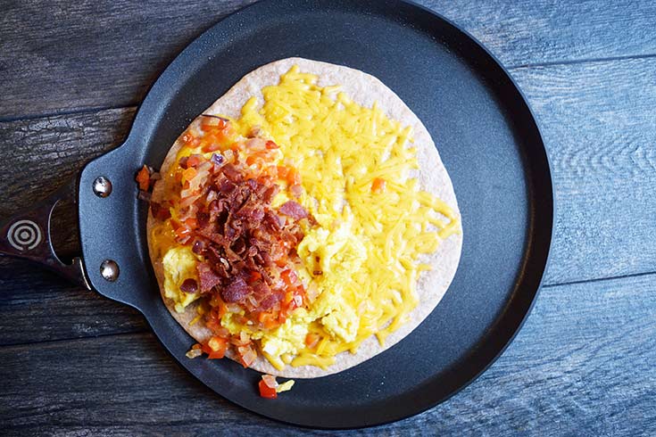 Sautéd vegetables and bacon bits added to a quesadilla with melted cheese, sitting in a skillet.