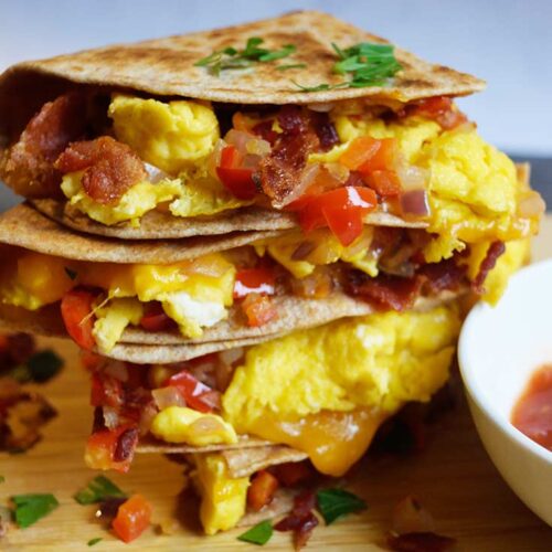 A stacked breakfast quesadilla sitting on a cutting board with fresh parsley sprinkled over the top.