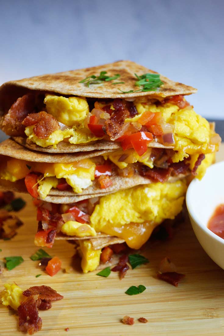 A stacked breakfast quesadilla sitting on a cutting board with fresh parsley sprinkled over the top.