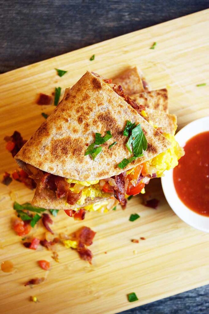 A cut and stacked Breakfast Quesadilla from overhead, sitting next to a white bowl of salsa.