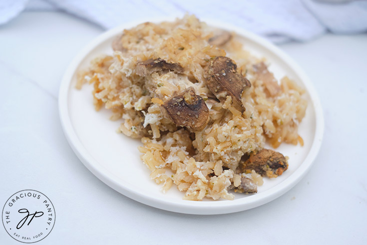 A white plate filled with brown rice mushroom casserole, sits on a white table.