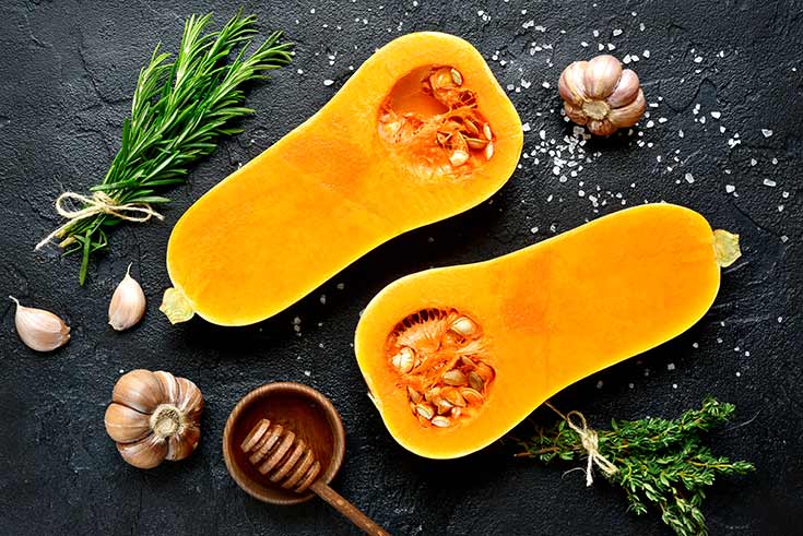 A butternut squash cut in half laying on a dark gray surface.