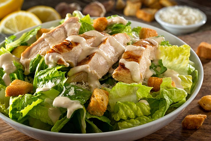 A white bowl filled with chicken caesar salad.