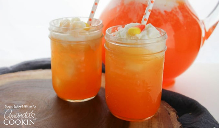 Two clear canning jars sit on a wood surface filled with candy corn punch.