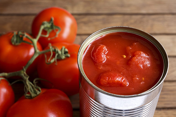 An opened can of canned tomatoes next to a bunch of fresh tomatoes.