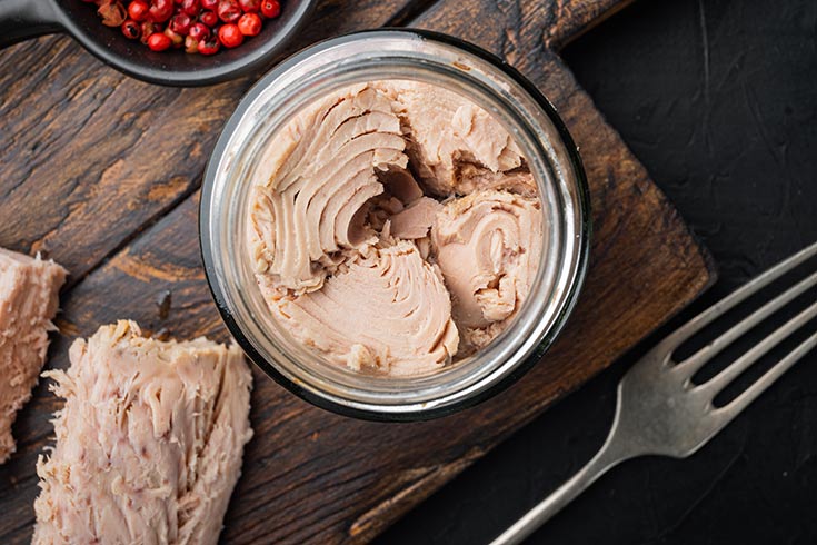 An open can of tuna with a fork laying next to it.