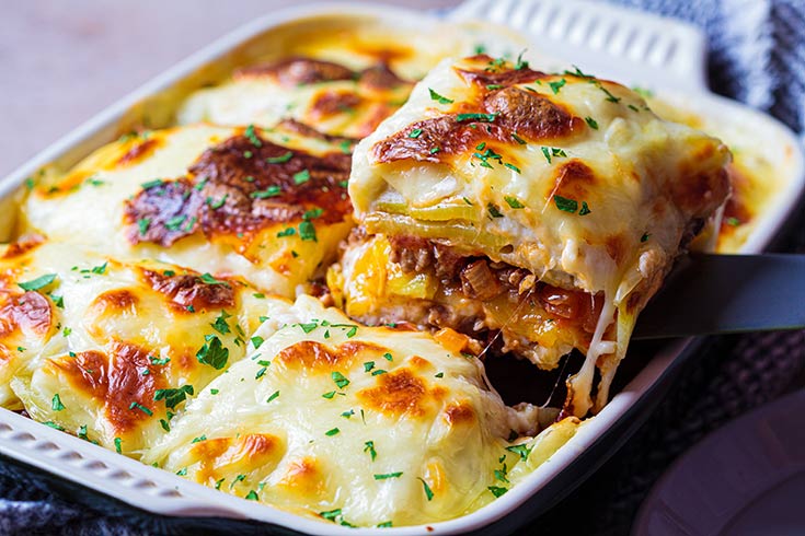 A cheesy casserole dish with a spatula lifting out a square-cut portion.