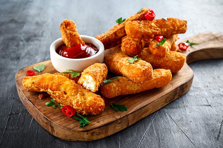 A cutting board holding a pile of cheese sticks and a small white bowl of marinara dip.