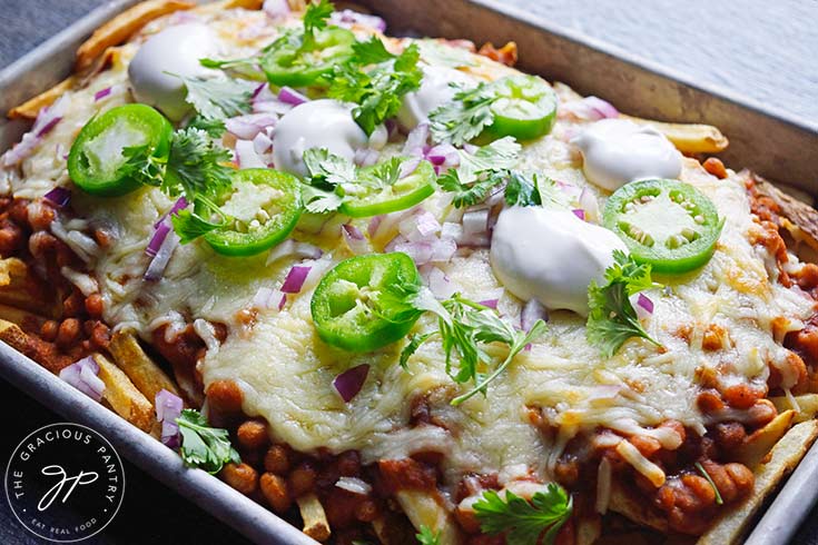 Chili Cheese Fries just out of the oven and garnished with dollops of sour cream, slices of jalapeno pepper, diced red onion, and fresh cilantro.