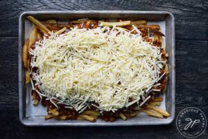 Grate cheese spread across chili and fries on a sheet pan.