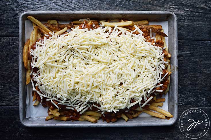 Grate cheese spread across chili and fries on a sheet pan.