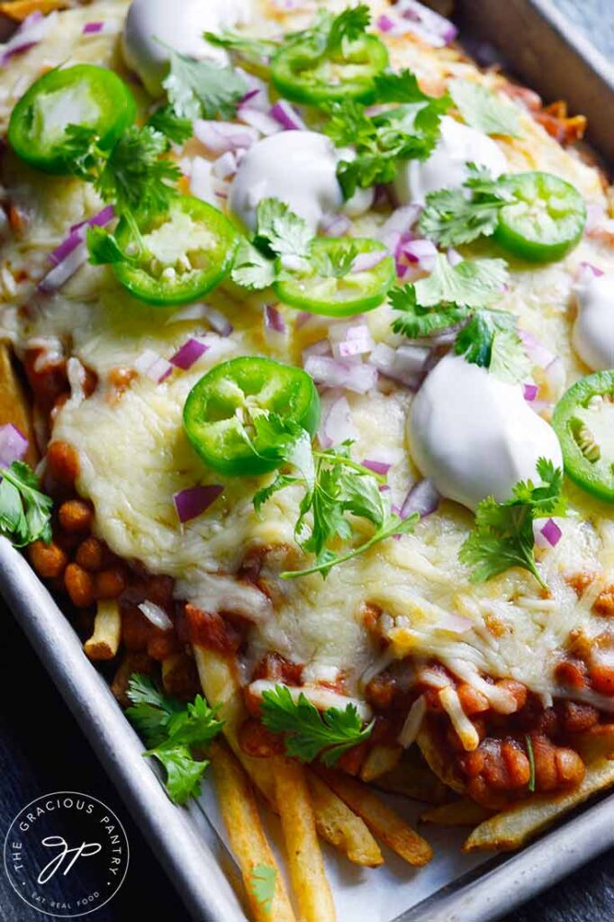 An overhead view of a sheet pan filled with garnished chili cheese fries.