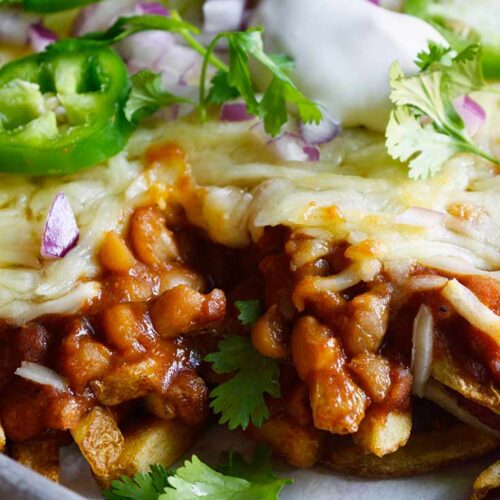 A sheet pan full of Chili Cheese Fries with a closeup of a corner portion removed.