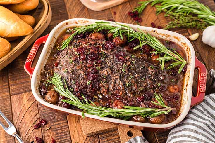 A casserole dish filled with cranberry holiday beef brisket and topped with fresh sprigs of rosemary.