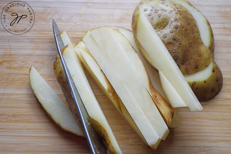 A knife cuts a potato into French fries.