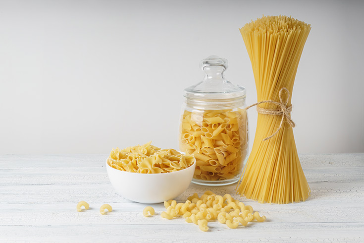 Four types of dry pasta sitting on a white surface.