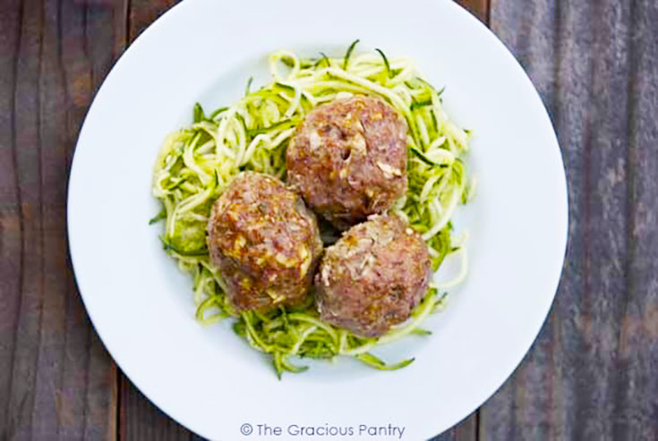 Three large meatballs on a bed of zucchini noodles on a white plate.